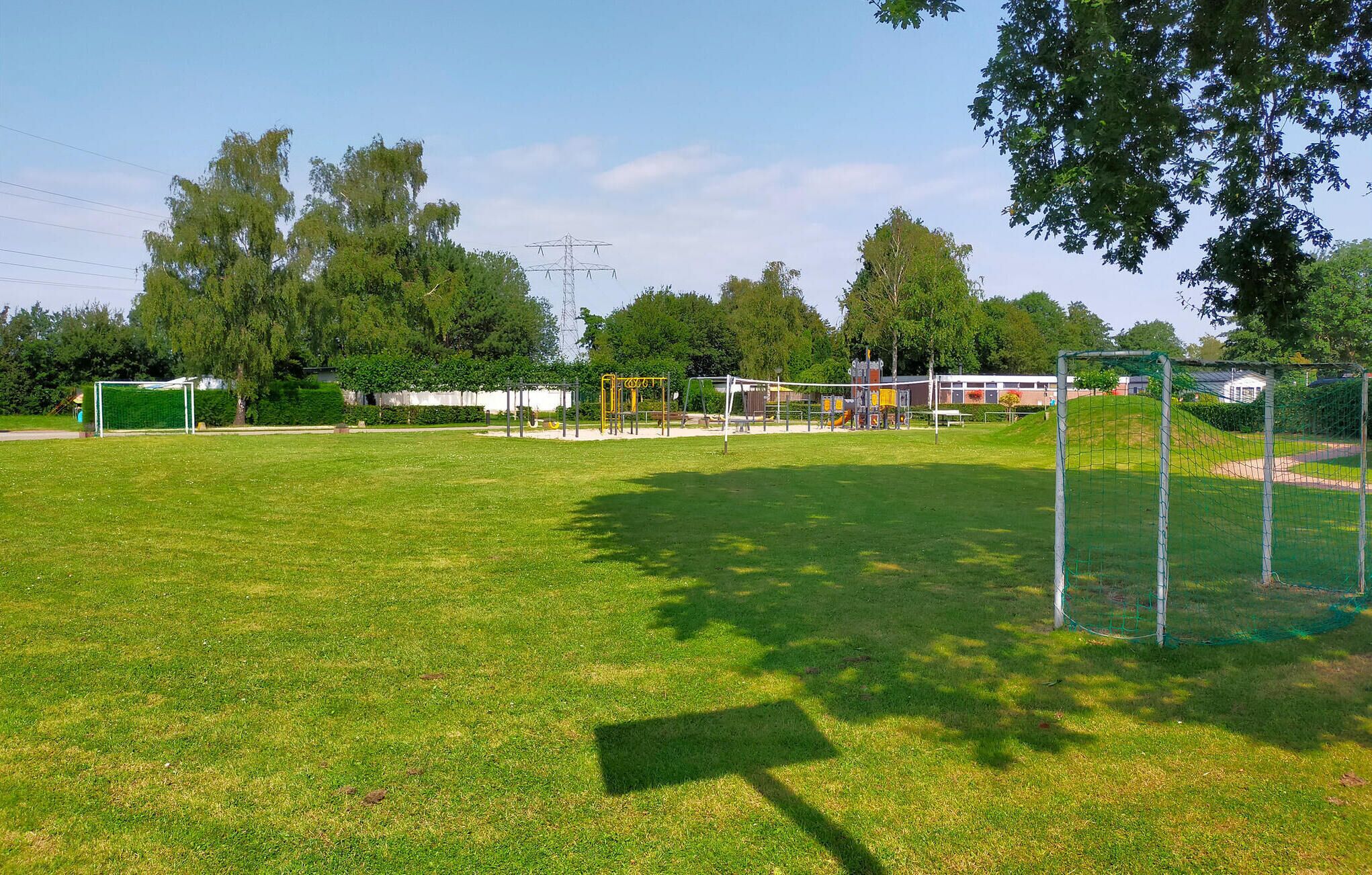 Un terrain herbeux avec un but de football, des jeux pour enfants et un bâtiment en arrière-plan.
