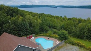 A backyard with a swimming pool, surrounded by lush greenery and a view of a large lake. - Owl's Head - Inground Pool - Spa - View - Méridien (Mansonville)