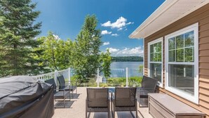 Eine Terrasse mit Gartenmöbeln, einem überdachten Grill und Blick auf einen See.
