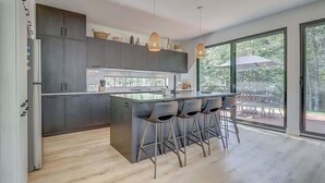 Una cucina moderna con isola centrale, sgabelli da bar e un'ampia porta scorrevole in vetro che dà su uno spazio esterno.