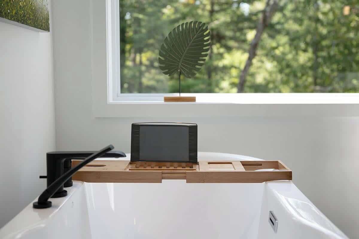 A white desk with a black monitor, wooden side table, and a leaf decoration on a window sill.