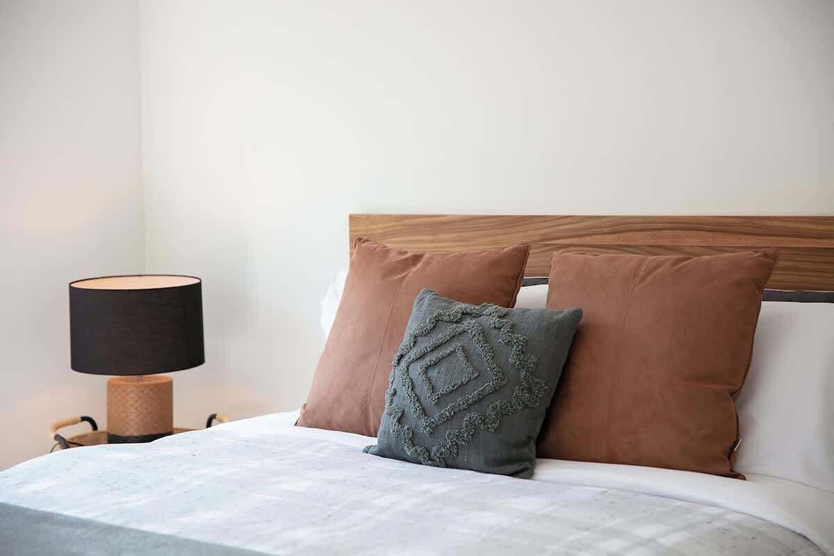 Een netjes opgemaakt bed met een houten hoofdbord, twee kussens en een bedlampje.
