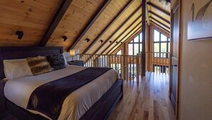 A bedroom with a large bed, wooden ceiling beams, and a view of a balcony.