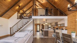 Un amplio salón con techos altos, vigas de madera, una escalera, una cocina y un comedor.