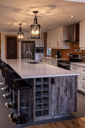 A modern kitchen with a large island, bar stools, stainless steel appliances, and pendant lighting.