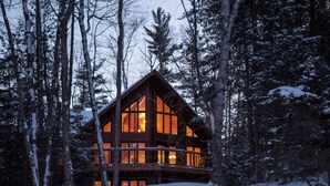 Una baita di legno con ampie finestre e un balcone, immersa in un paesaggio di alberi coperti di neve.