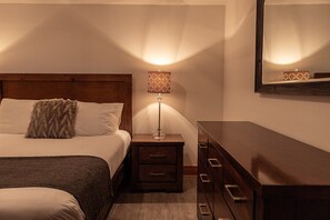 Una habitación de hotel con cama, mesita de noche, lámpara, cómoda y espejo.