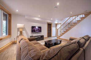 Una sala de estar moderna con un sofá grande, un televisor y una escalera.