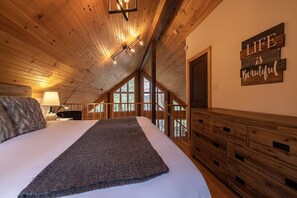 A bedroom with a large bed, wooden ceiling, and a window with a view of trees.