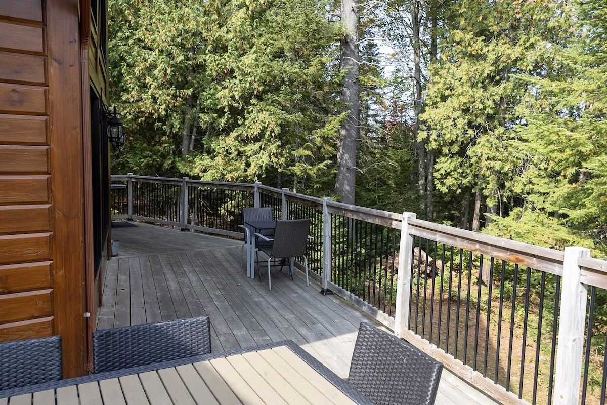 A wooden deck with a railing, outdoor furniture, and a view of a forested area.