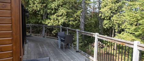 A wooden deck with a railing, outdoor furniture, and a view of a forested area.
