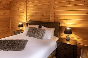 A wooden-paneled room with a bed, two bedside lamps, and a nightstand.