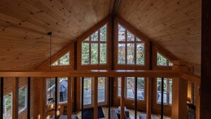 Una baita con soffitto alto, ampie finestre e vista sulla natura.
