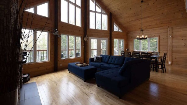 A spacious living room with a large sectional sofa, wooden floors, and large windows allowing natural light.