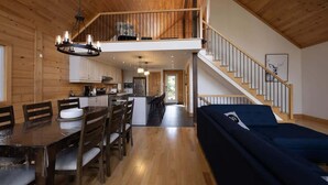 A spacious living area with a dining table, chairs, a sofa, a staircase, and a kitchen in the background.