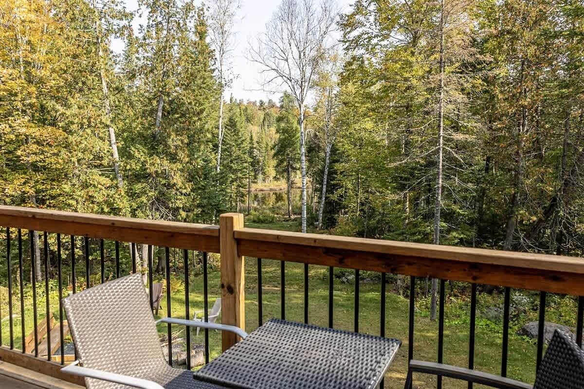 Une terrasse en bois avec deux chaises et une table, donnant sur une zone boisée.