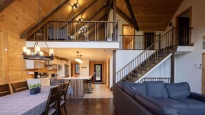 Un vaste espace de vie de style loft, doté d’un plafond haut, d’une table à manger avec des chaises, d’un canapé et d’un escalier menant à un niveau supérieur.
