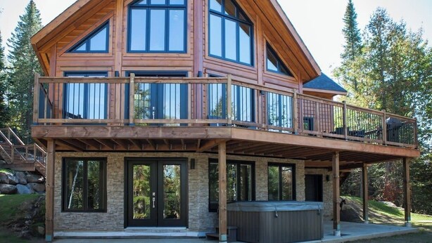 Une cabane en rondins à deux étages, dotée d’un balcon et d’un jacuzzi.