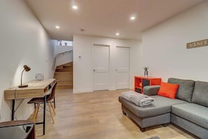 Un salon moderne avec un canapé gris, un bureau en bois et un escalier menant à un deuxième étage.