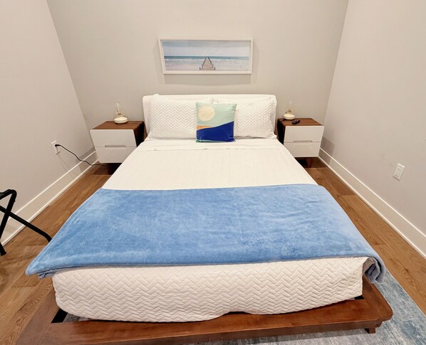 Een slaapkamer met een bed, twee nachtkastjes, een wanddecoratie en een houten vloer.