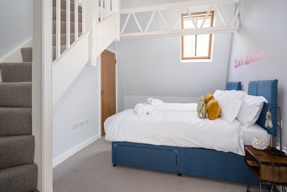 A bedroom with a bed, a nightstand, a lamp, a window, and a staircase.