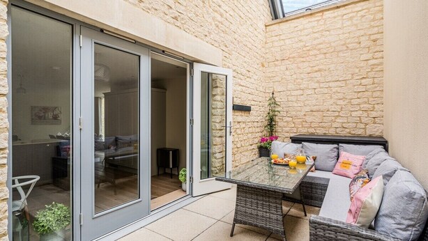 A patio with a glass door leading to a room, a wicker sofa, and a table with fruits and a plant. - The Corner House - modern 3-bedroom city home (Bath)