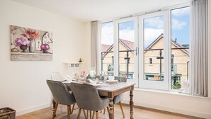 A dining area with a wooden table, grey chairs, and a large window with a view of buildings. - The Corner House - modern 3-bedroom city home (Bath)