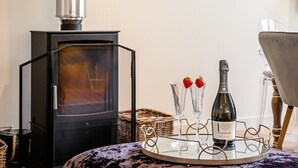 A cozy room with a wood-burning stove, a glass table with a bottle of wine and two glasses, and a chair. - The Corner House - modern 3-bedroom city home (Bath)