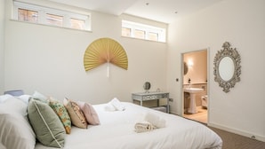 A neatly made bed with pillows, a wall fan, a mirror, and a bathroom visible through an open door. - The Corner House - modern 3-bedroom city home (Bath)