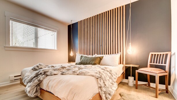Un dormitorio moderno con una cama de madera, un plaid de piel, una silla y un diseño de pared con listones.