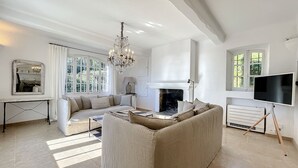 A spacious living room with a large beige sofa, a chandelier, a fireplace, and a television. - Charming villa with garden and heated pool, perfect families (Saint Paul de Vence)