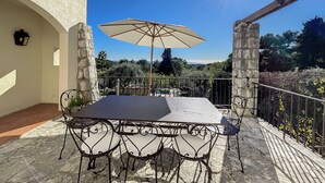 A patio with a table and chairs, an umbrella, and a view of the landscape. - Charming villa with garden and heated pool, perfect families (Saint Paul de Vence)