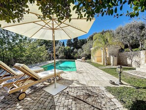 Ett poolområde med solstolar, en pergola med ett tak och en stenmur.