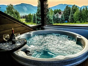 A hot tub with a mountain view, a bottle of wine, and two glasses on a checkered tablecloth. - "Living The Dream" Townhome w Romantic Hot Tub for 2 Facing Mt. Crested Butte (Crested Butte)