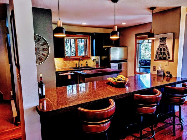 A modern kitchen with a central island, bar stools, pendant lighting, and a large window. - "Living The Dream" Townhome w Romantic Hot Tub for 2 Facing Mt. Crested Butte (Crested Butte)