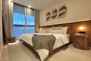 Un dormitorio moderno con una cama grande, una mesita de noche y vistas al exterior a través de una ventana con cortinas.