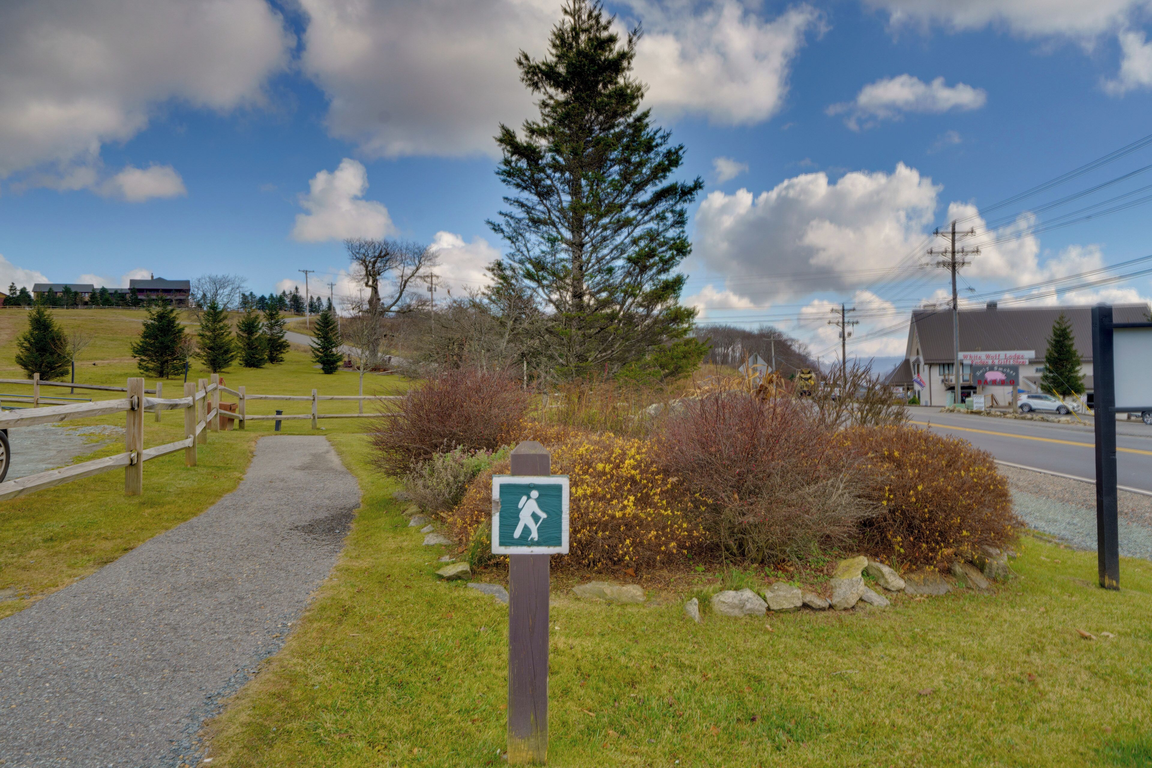 A hiking trail sign in a grassy area with a paved path, surrounded by trees and bushes.
