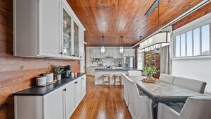 A modern kitchen with wooden ceiling, white cabinets, and a central island with stools.