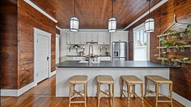 A kitchen with a large island, white cabinets, hanging pendant lights, and a wooden ceiling.