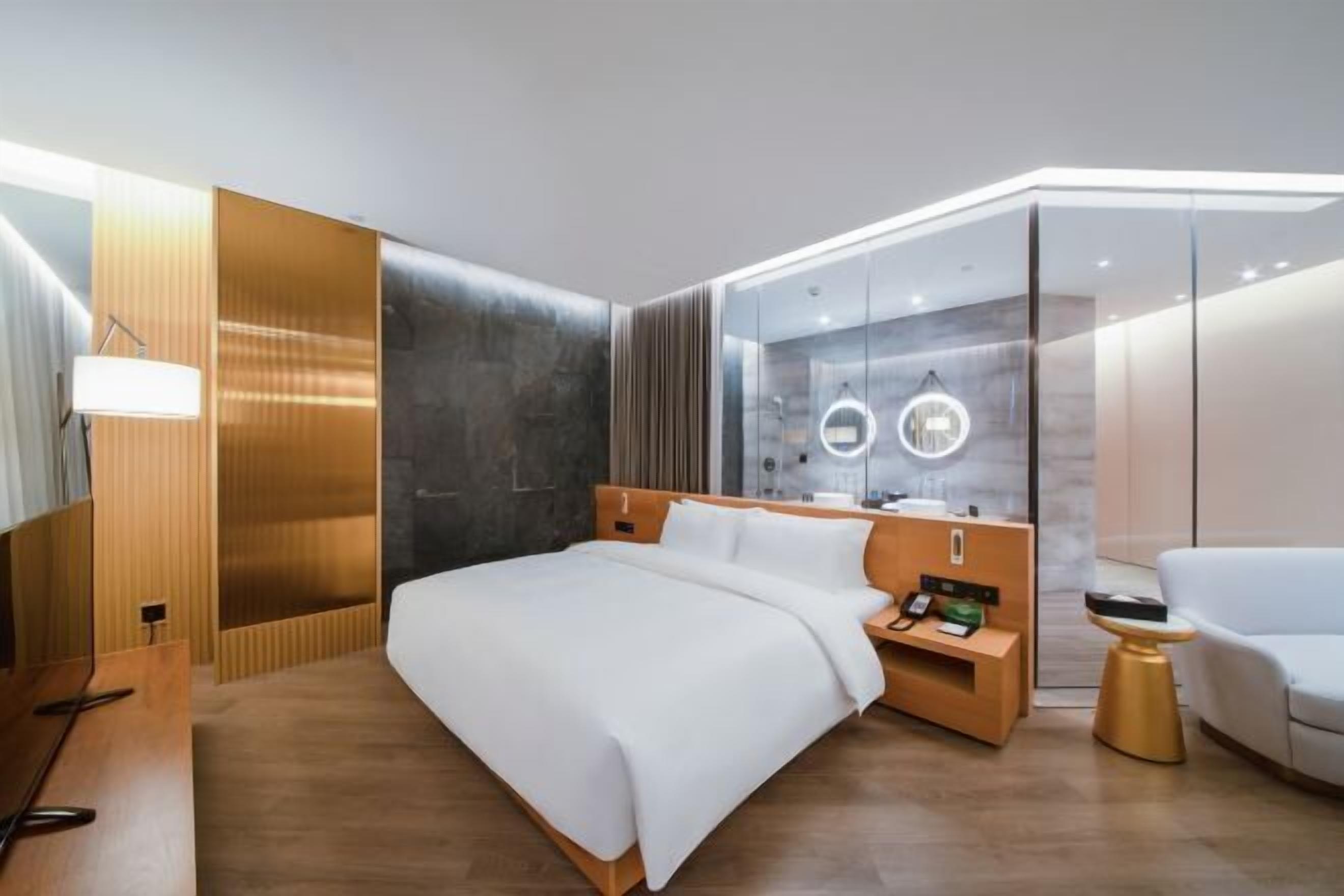 A modern hotel room with a large bed, bedside tables, a wardrobe, and a seating area.