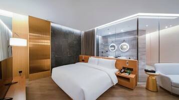 A modern hotel room with a large bed, bedside tables, a wardrobe, and a seating area.