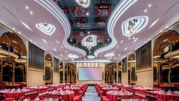 A banquet hall with tables set for dining, a large screen at the front, and ornate ceiling design.