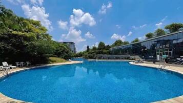 A large, clear swimming pool with lounge chairs and a modern building in the background.