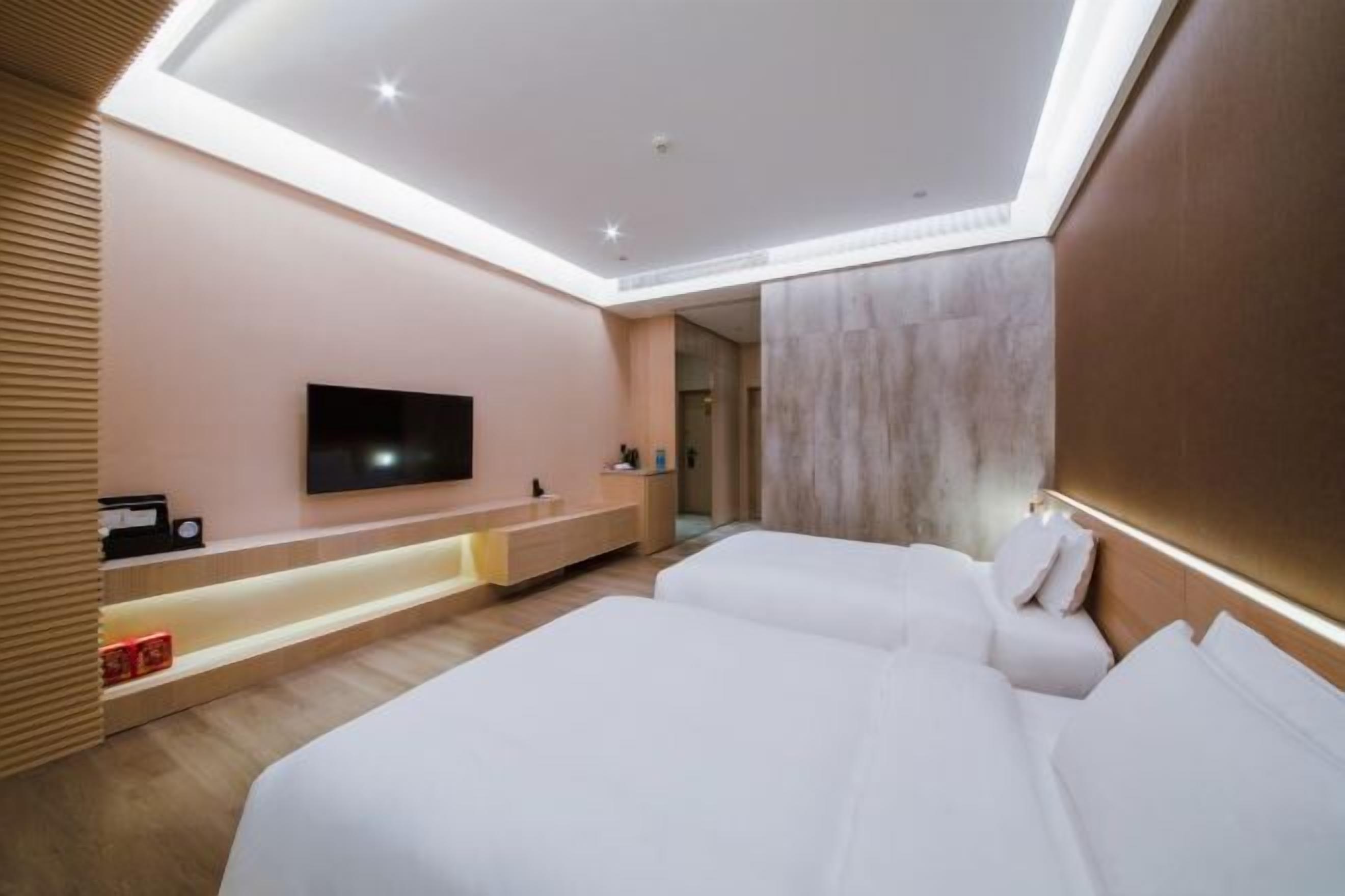 Une chambre d’hôtel moderne dotée d’un téléviseur à écran plat fixé au mur, d’une table de chevet, d’une banquette intégrée et d’un grand lit avec une literie blanche.