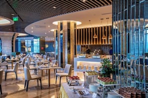 A modern dining area with tables and chairs, a counter with food items, and a kitchen in the background. - Like Hotel (Guiyang)