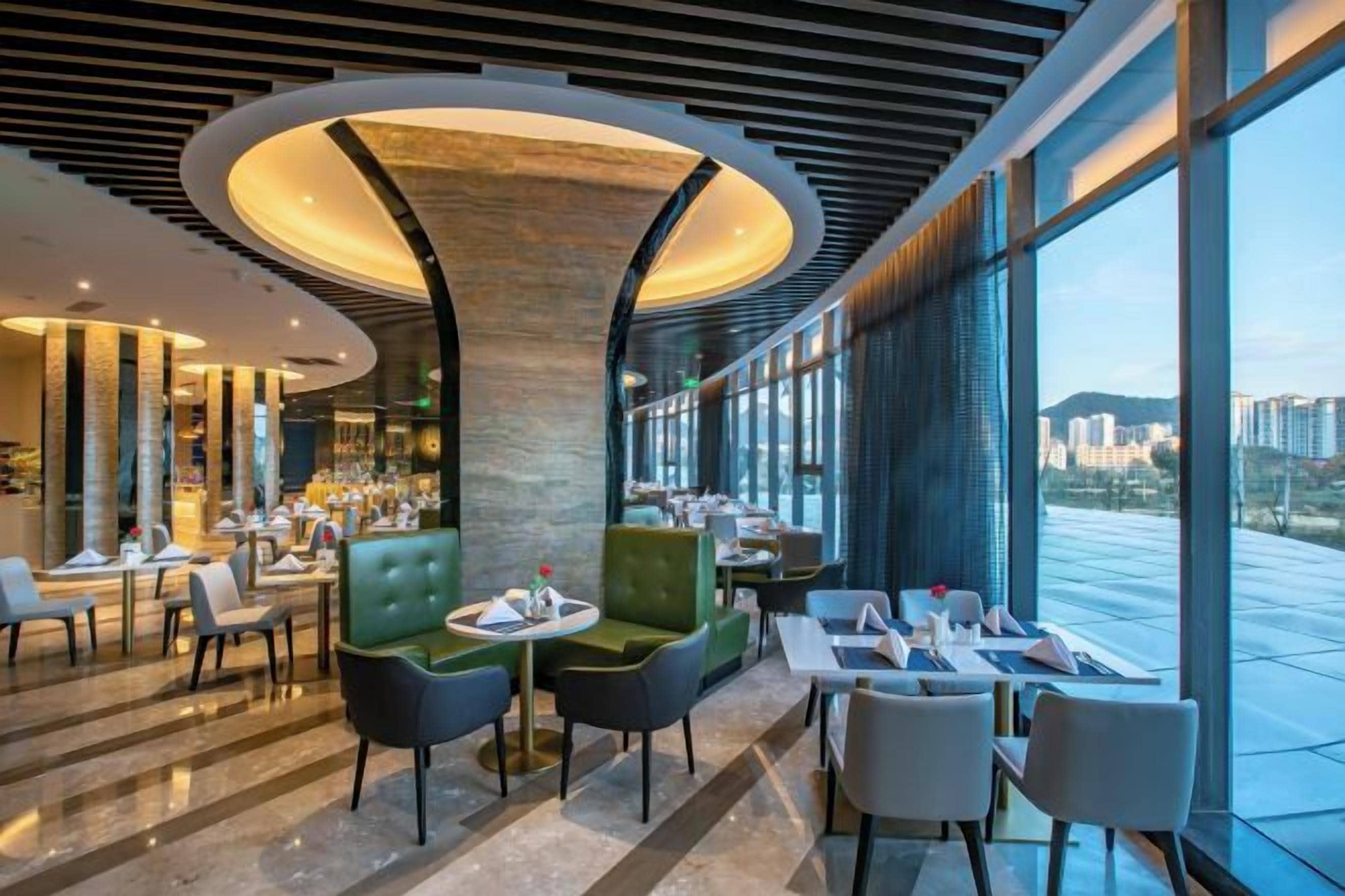 A modern restaurant with a central column, seating arrangements, and a view of the cityscape.