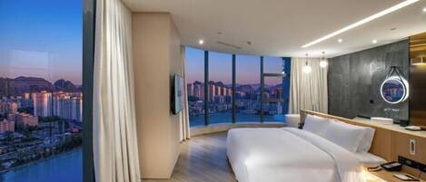 Una habitación de hotel moderna con una cama grande, un escritorio, un tocador y vistas a un paisaje urbano.