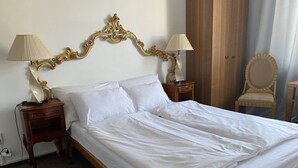 A neatly made bed with white linens, two bedside tables with lamps, a wooden chair, and a wooden wardrobe.