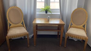 Two wooden chairs with gold trim and beige cushions, a small wooden table, and a potted plant on a windowsill.