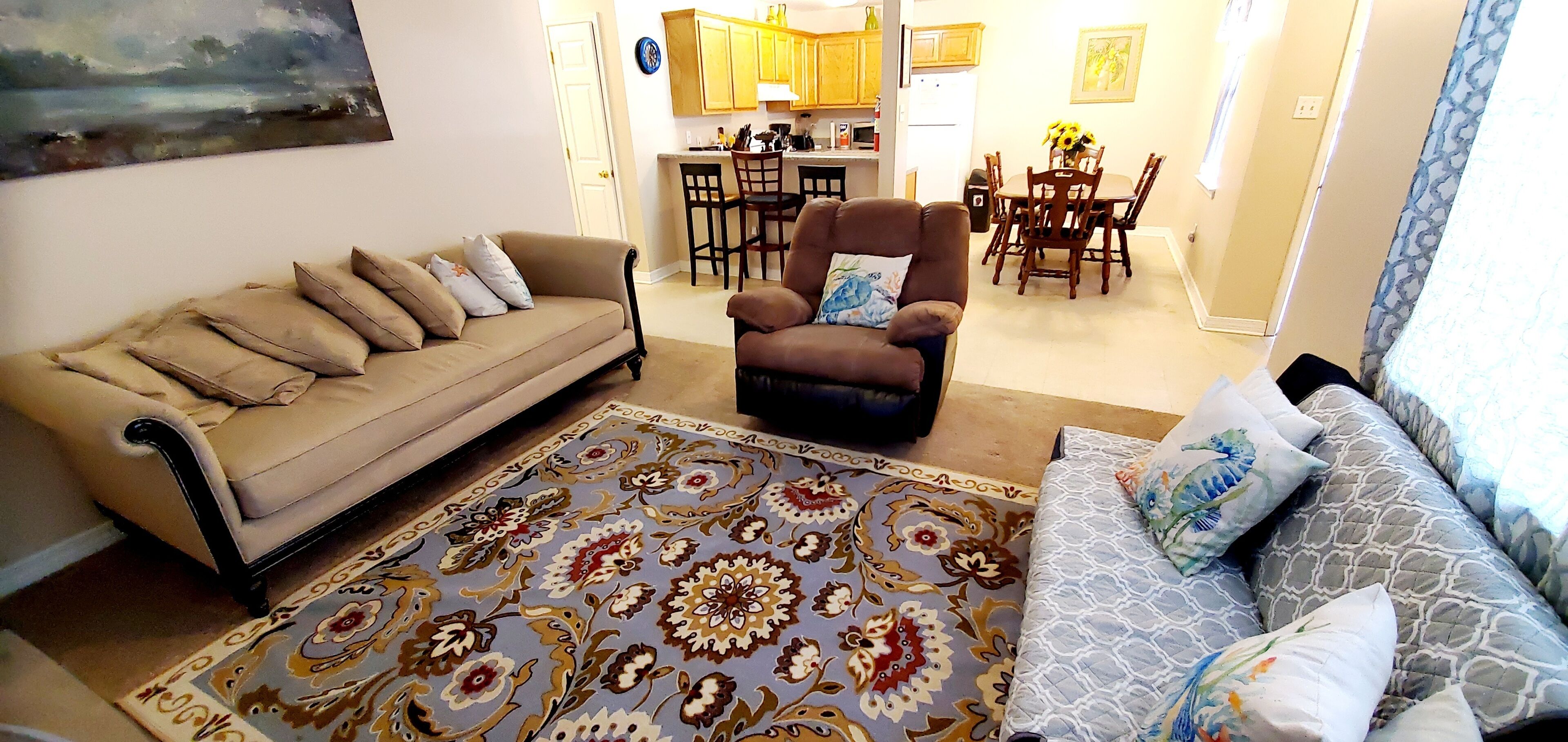 Un salon avec un canapé beige, un fauteuil marron et un tapis à motifs.